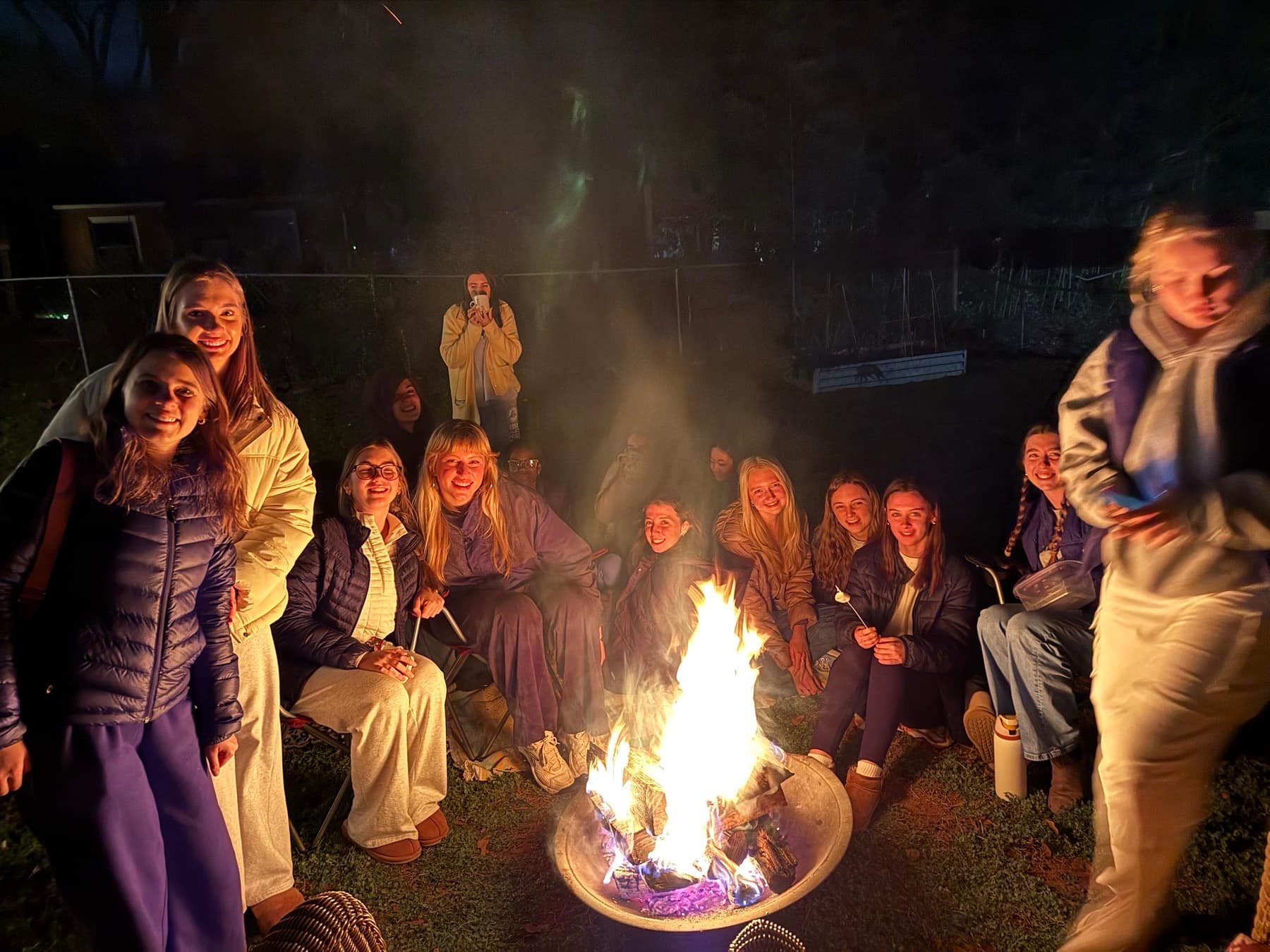 Freshman women smiling together beside a bonfire